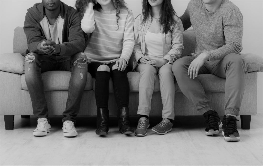 Black and white photo of four teenagers sitting on a couch together.