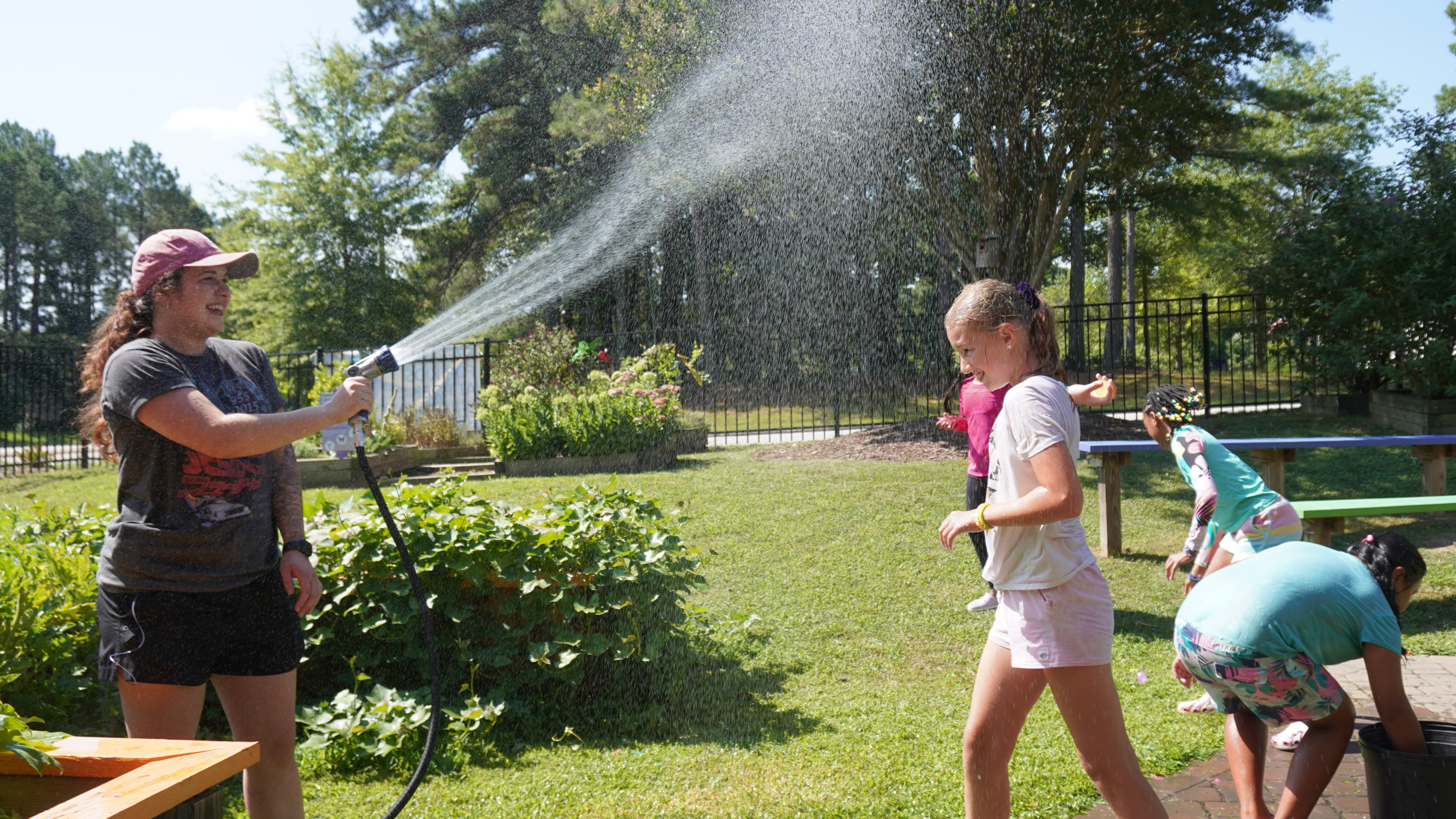 Camp counselor spraying camper with sprinkler. Child is smiling and playing under the water.
