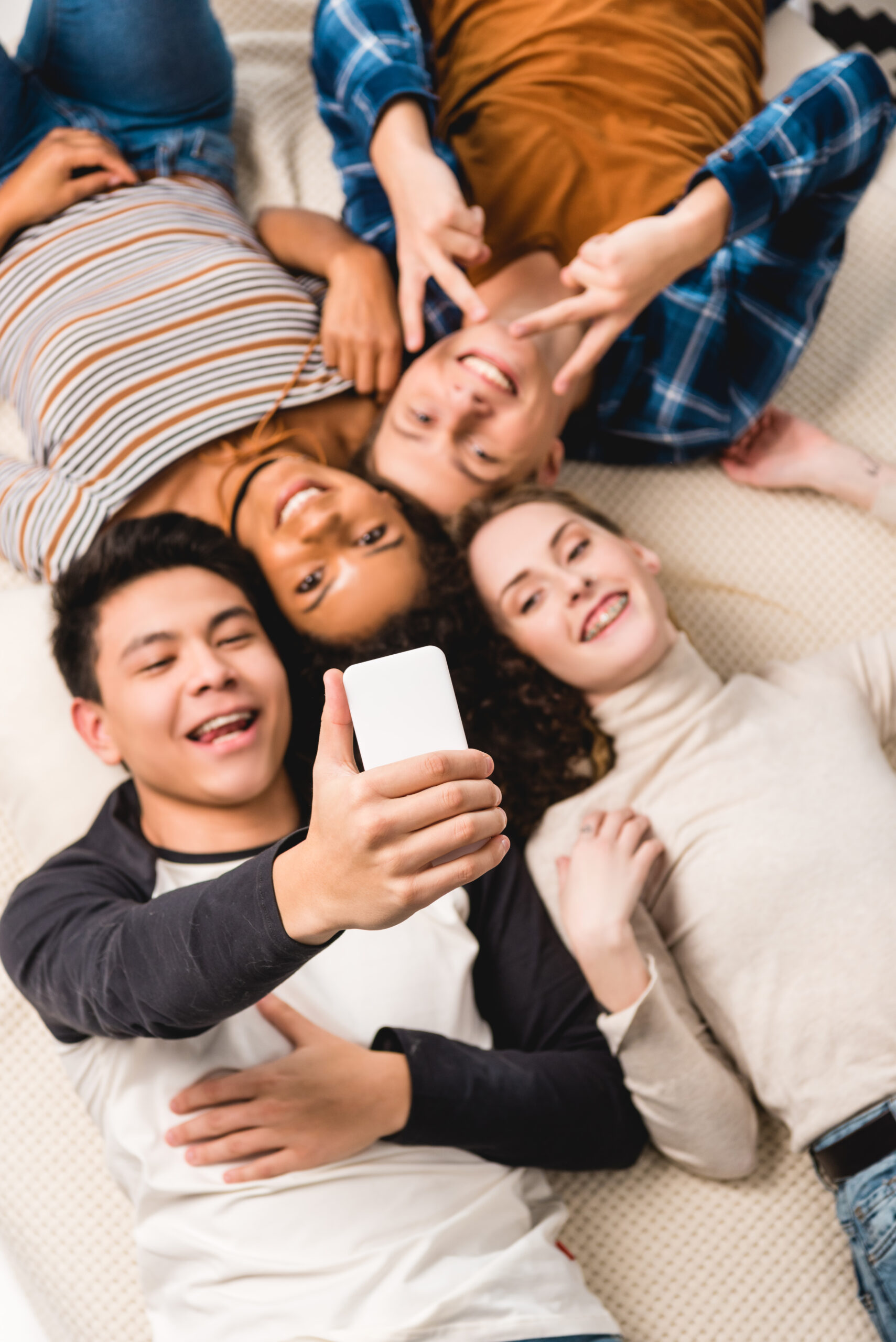 Several teenaged friends lie in a circle on the floor smiling at the camera above